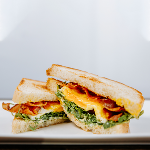 il porcellino salumi's Breakfast BLT sandwich on a plate and cut in half to show the ingredients cooked egg yolk oozing out.