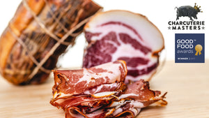 A picture of il porcellino salumi's Coppa cut into slices and whole muscle Coppa chubs in the background. The Charcuterie Masters grand champion seal and Good Food Awards 2017 winner seal are on the picture.