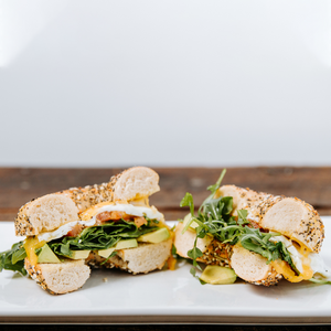 il porcellino salumi's Everything Bagel Vegetarian Breakfast Sandwich cut in half and displayed on a plate to show the sandwiches ingredients.