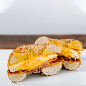 il porcellino salumi's Everything Bagel Pork Roll Breakfast sandwich on a plate. The sandwich is cut in half and pictured to show the cross section of ingredients.