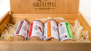 Four different il porcellino salumi salami flavors resting on decorative filling in a wood branded gift box.