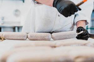 A picture of freshly stuffed salami chubs and the hands of an il porcellino salumi staff member tying them with butcher twine.