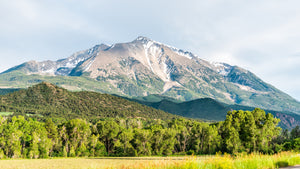 Mt. Sopris in Colorado with light grey clouds above and beautiful green summer colors highlighted by the sun beams.