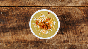 A cup of soup on a wood table and pictured from above to represent il porcellino salumi's soup du jour.