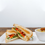 il porcellino salumi's "The Wook" sandwich cut in half and positioned to display the cross section of each half and next to a cup of soup.
