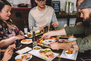 Four people sitting around a table full of plates of food eating and reaching to grab food from different plates on the table.