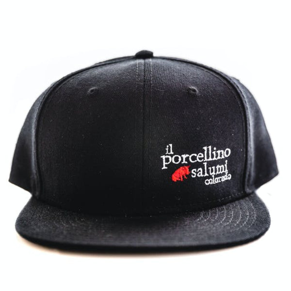 A black baseball hat positioned with the brim facing the camera. Il porcellino salumi's logo is on the front left of the hat.