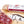Load image into Gallery viewer, A close up of saucisson sec salami in packaging and on a cutting board with blurred salami slices, herbs and spices in the foreground.
