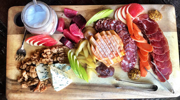 A fall harvest inspired charcuterie board shot from above. The board contains different cheese, cured meats, season fruits and veggies, and candied walnuts.