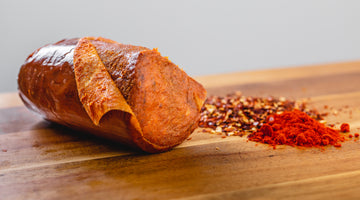 A close up side shot of 'nduja salami on a cutting board with spices next to it.