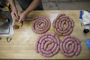 A picture of several sausages on a table while more sausage is being made with a casing stuffer.