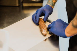 Salami being placed on butcher paper to be hand wrapped and packaged.