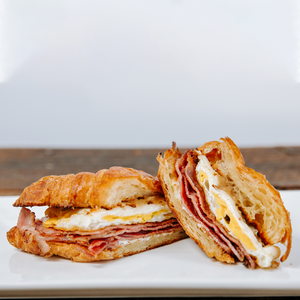 il porcellino salumi's Ham & Cheese Breakfast Croissant cut in half and displayed on a plate to show the cross section and ingredients.