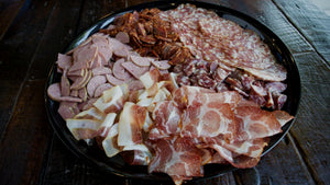 A large platter filled with different types of cured meat like summer sausage, salami, prosciutto and coppa, and displayed on a wood table.