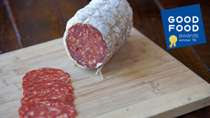 A large format chub of il porcellino salumi's Pepperoni on a cutting board and pictured from an angle with Pepperoni slices in the foreground.