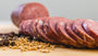 A closeup of il porcellino salumi Summer Sausage slices, herbs and spices, and a whole summer sausage chub in the background.