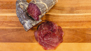 Slices and two whole chubs of il porcellino salumi's Wagyu Beef Bresaola pictured from above on a cutting board. 
