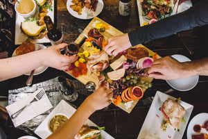 A picture looking down at a table with plates of food, a charcuterie board in the middle and hands reaching to grab food.