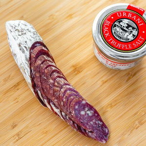 il porcellino salumi's black truffle salami pictured from above and cut into slices on a cutting board next to a jar of black truffle salt.