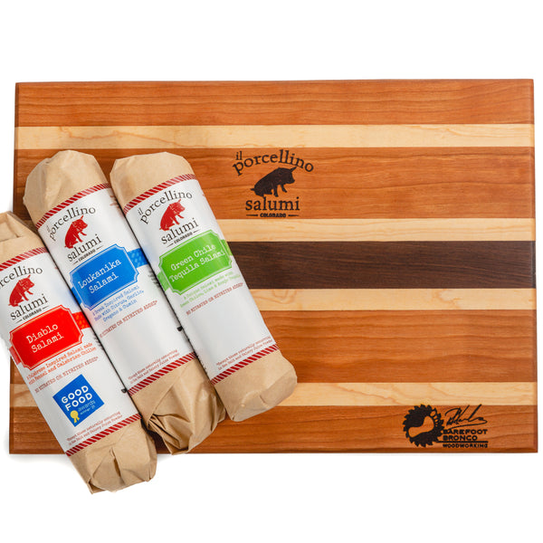 A product photo of a cutting board branded with the il porcellino salumi and barefoot bronco logos and with three wrapped salami flavors on it.