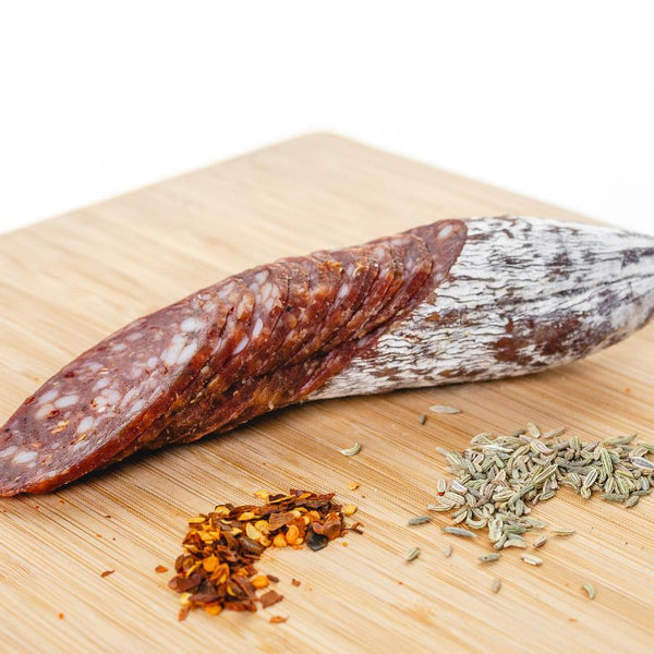 A picture of a spicy salami called Diablo salami by il porcellino salumi shot from the side and cut into slices on a cutting board.