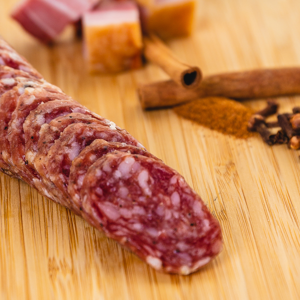 A close up of bacon whiskey salami with herbs and spices in the background.