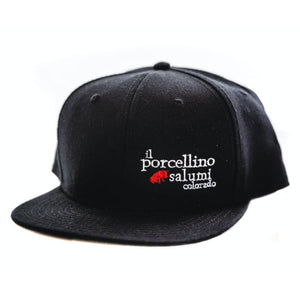 A black baseball hat with il porcellino salumi's logo on it facing the camera at a slight angle.