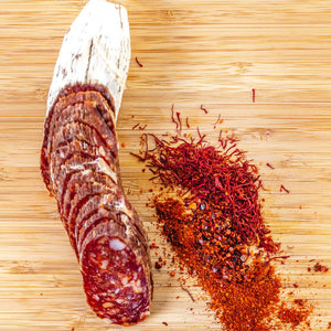 Hard Saucisson Basque Salami with half cut into slices on a cutting board next to herbs and spices.