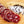 Load image into Gallery viewer, A close up of salami slices displaying the fat marbling, herbs and spices. The salami slices are on a wood cutting board with herbs and spices blurred in the background.
