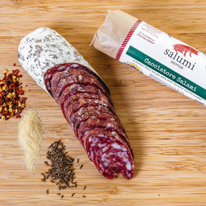 A picture from above of Cacciatore salami in packaging and cut into slices on a cutting board next to herbs and spices.