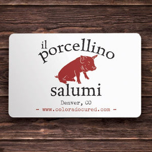 A picture of a gift card with the words "il porcellino salumi, Denver, CO" on it with a wood grain background.