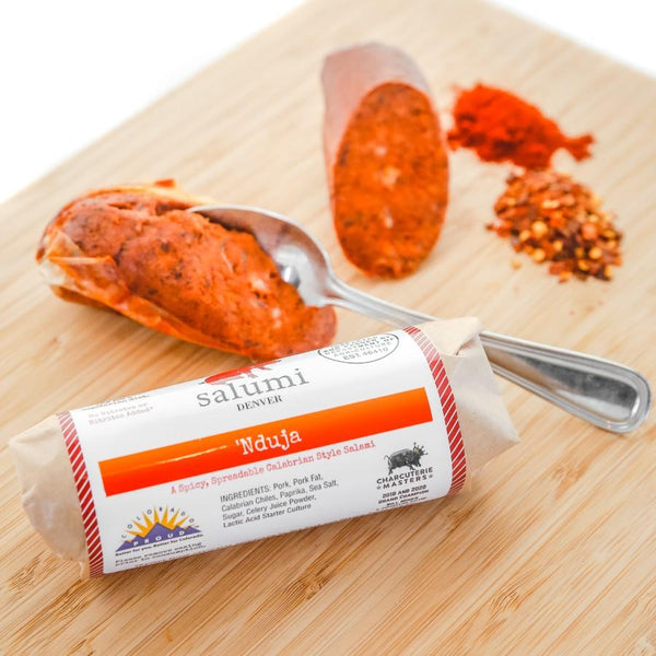 A product photo of il porcellino salumi's 'Nduja salami on a cutting board in packaging and non packaged chubs.