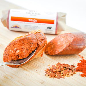 'nduja salami on a cutting board with a spoon in the salami to show how soft it is.